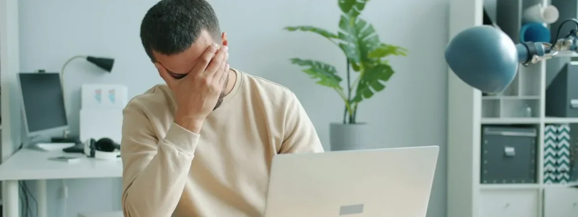 Tired man rubbing his face while sitting in front of a laptop