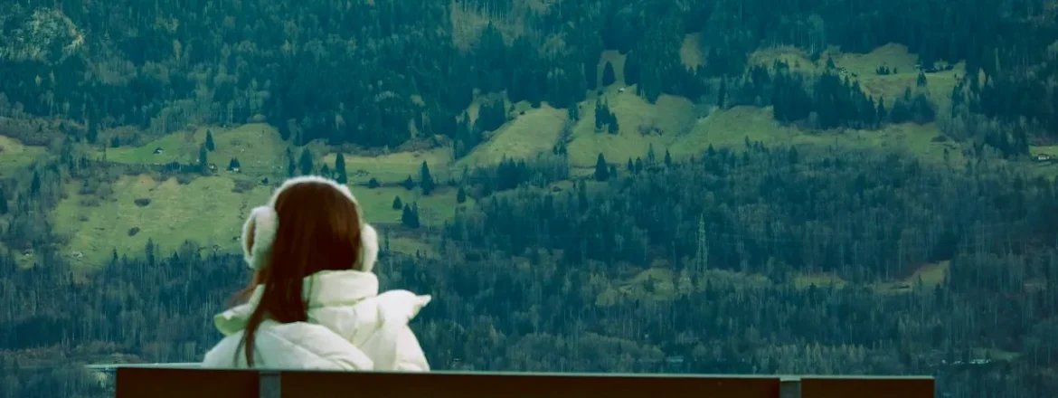 Woman sitting alone on a bench beside a lake, looking out over the water