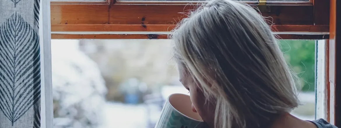 Woman holding a drink and looking calmly out of a bright window